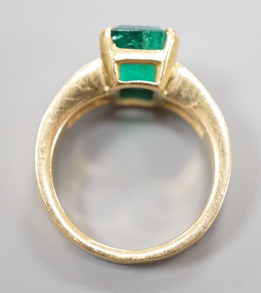 A modern yellow metal and single stone emerald set dress ring, with graduated baguette cut diamond set shoulders, size M/N, gross weight 7.3 grams.